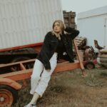 woman in black jacket and white pants sitting on brown wooden bench