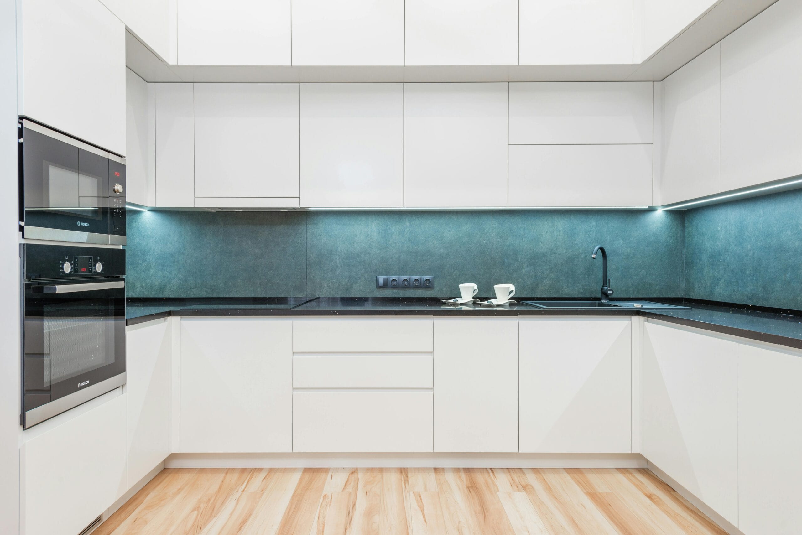 Interior of white modern kitchen with minimalist design of white cabinets blue backsplash and black built in appliances