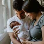 woman holding baby beside man smiling